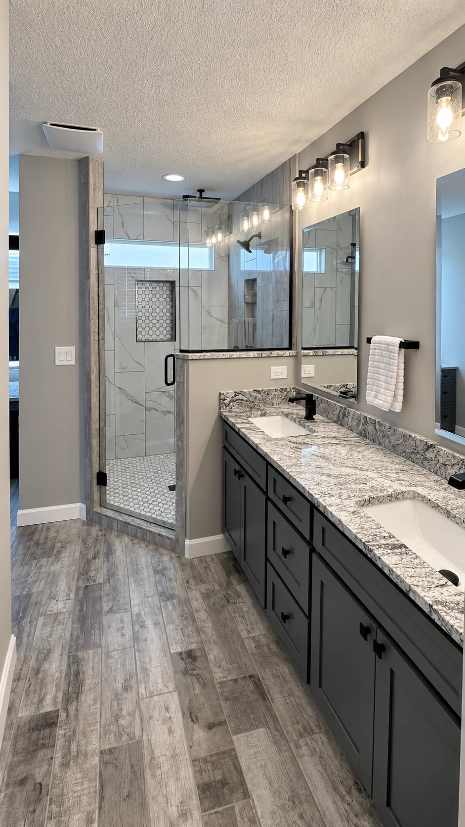 Dark double vanity with patterned counters beside a glass shower and high window