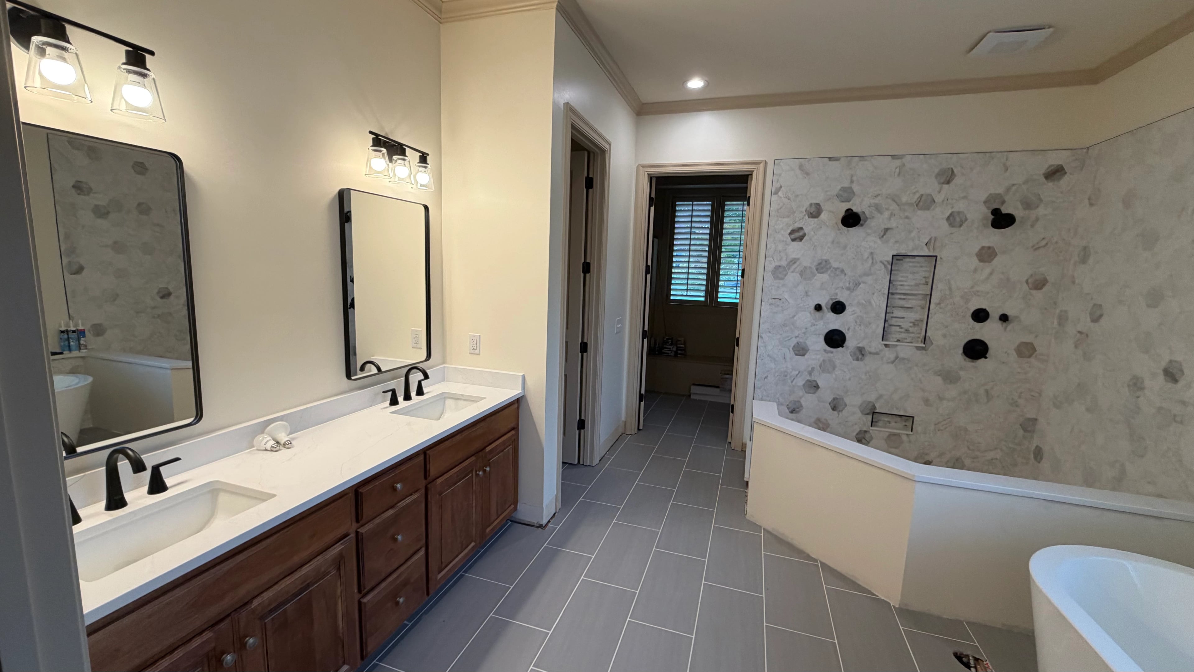 Wood double vanity and paired mirrors beside a tiled shower wall