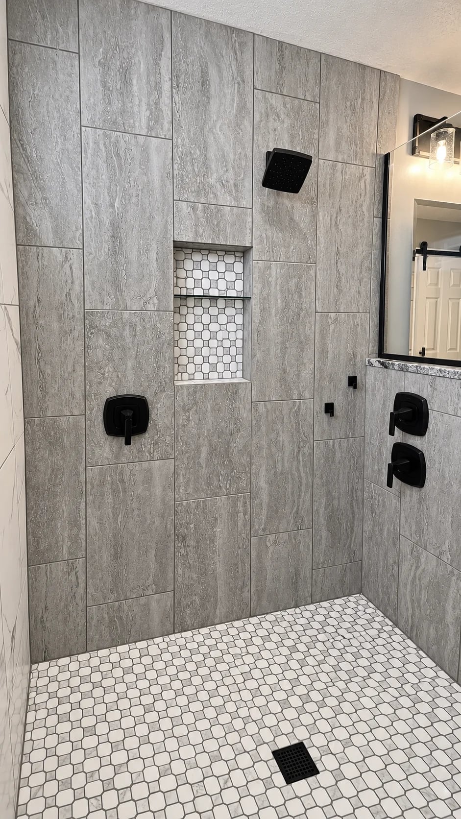 Gray tiled shower with dark fixtures, a recessed shelf and small-pattern floor tile