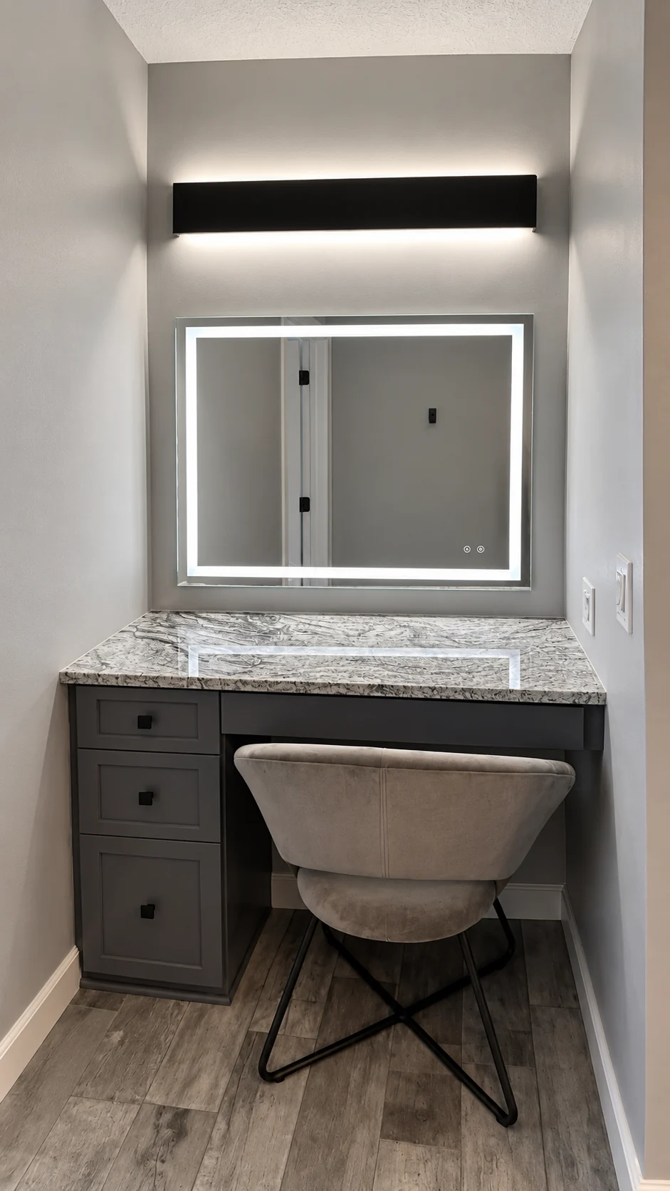 Seated makeup vanity with dark drawers and an illuminated rectangular mirror