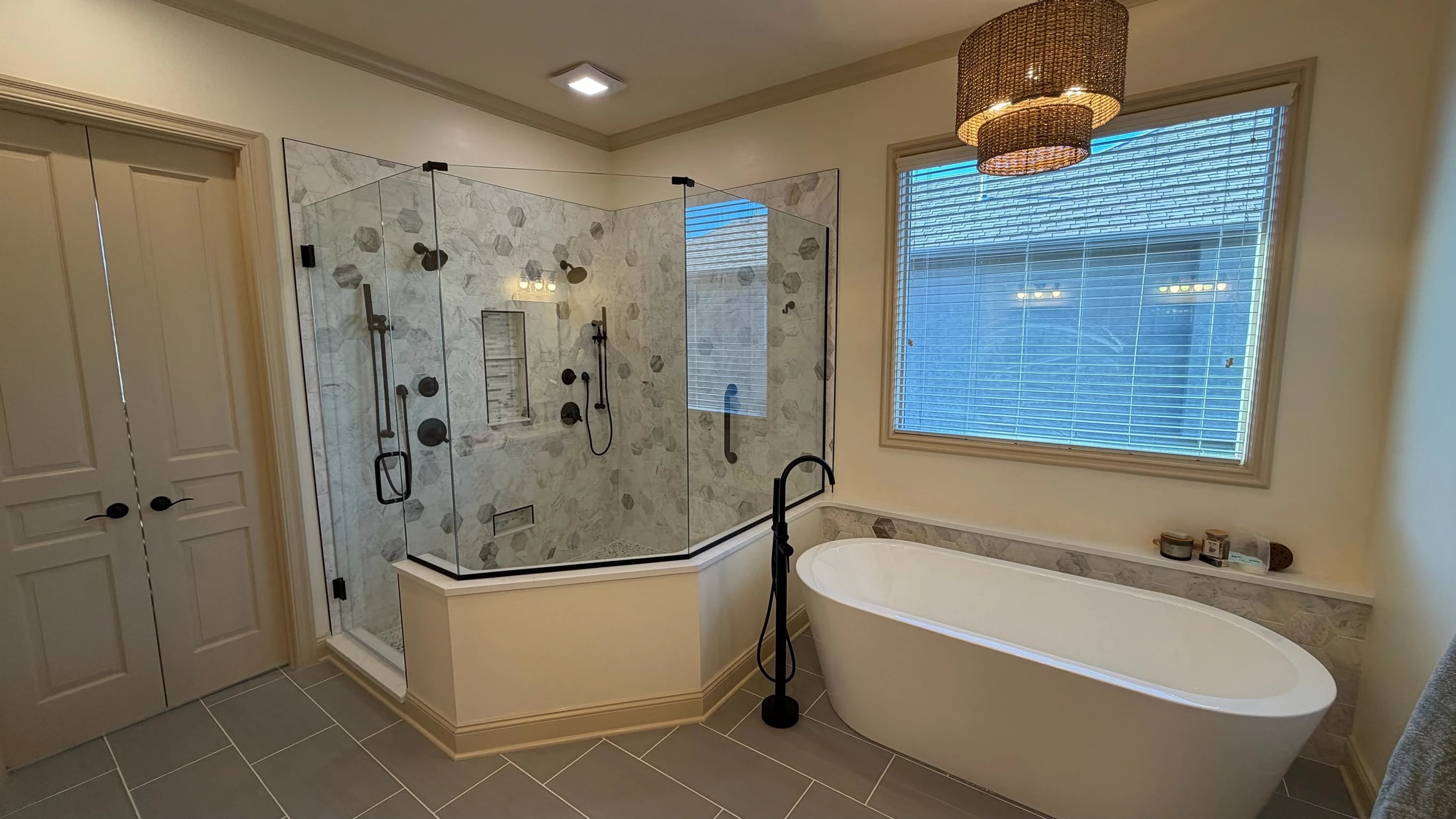 Freestanding tub beside a glass corner shower with patterned marble-look tile
