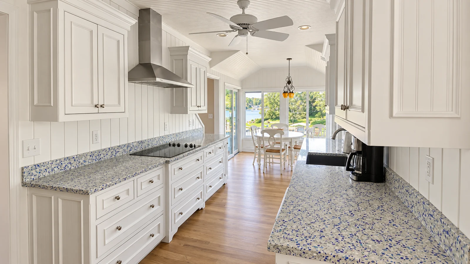 White galley kitchen with blue-flecked counters opening toward a lake-facing dining area