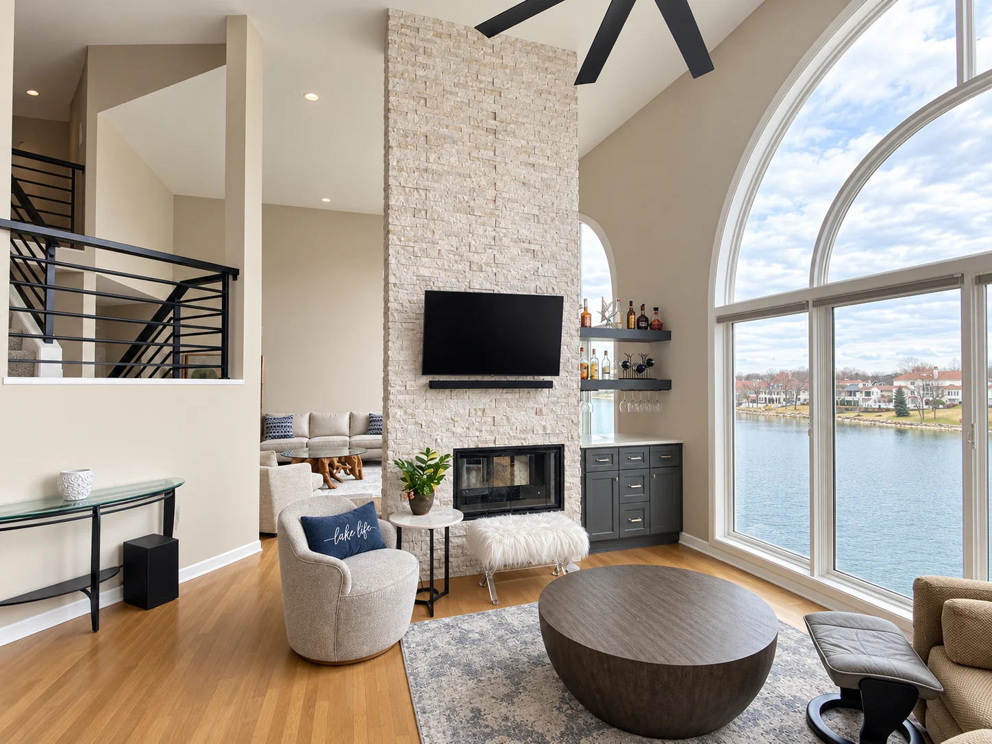 Tall stone-faced fireplace, arched lake-facing window and adjoining living space