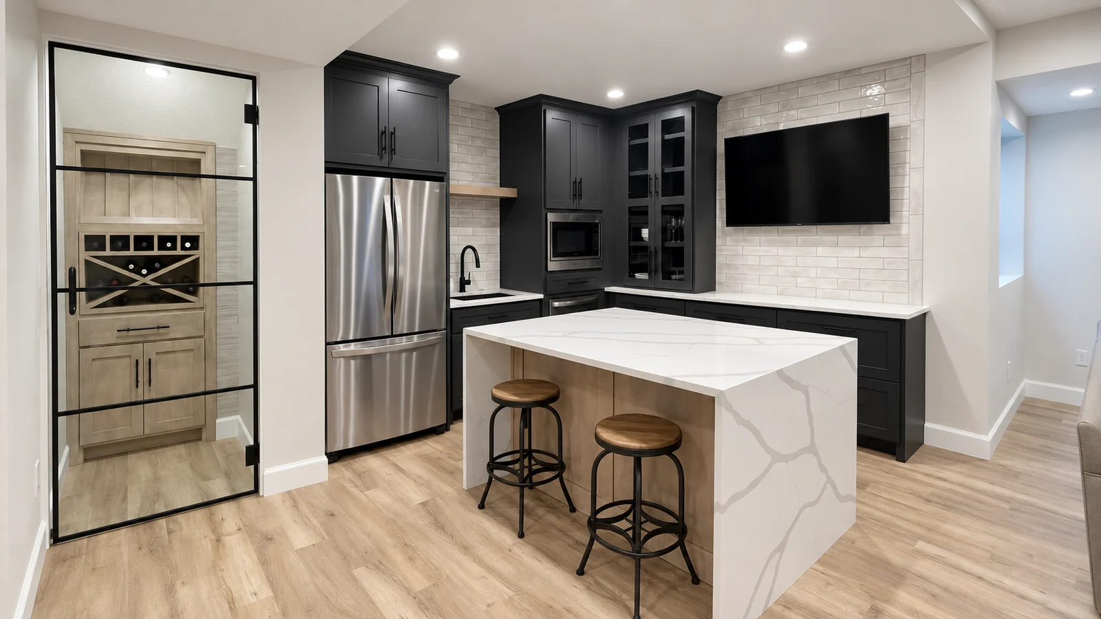 Dark basement kitchen cabinets and waterfall island beside a glass-door wine nook