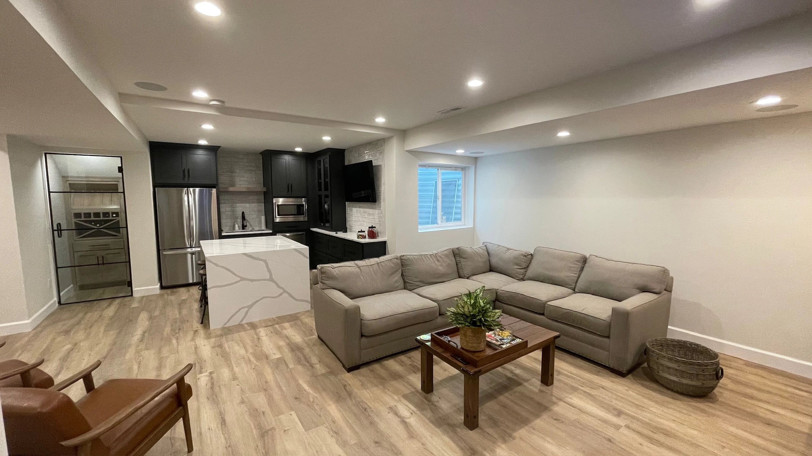 Sectional seating connected to a basement kitchen, island and glass-door wine nook