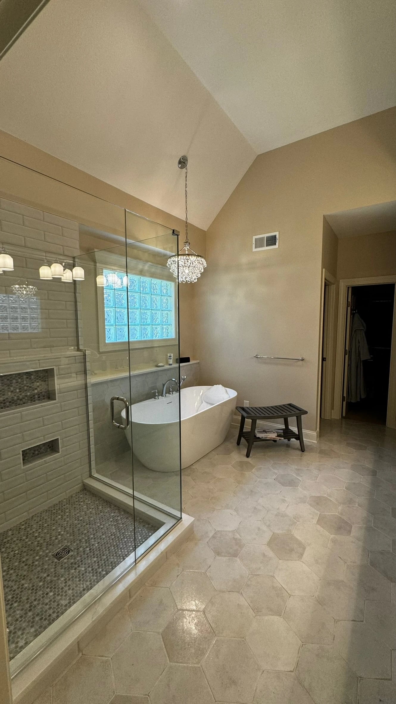 Glass shower beside a freestanding tub beneath a glass-block window