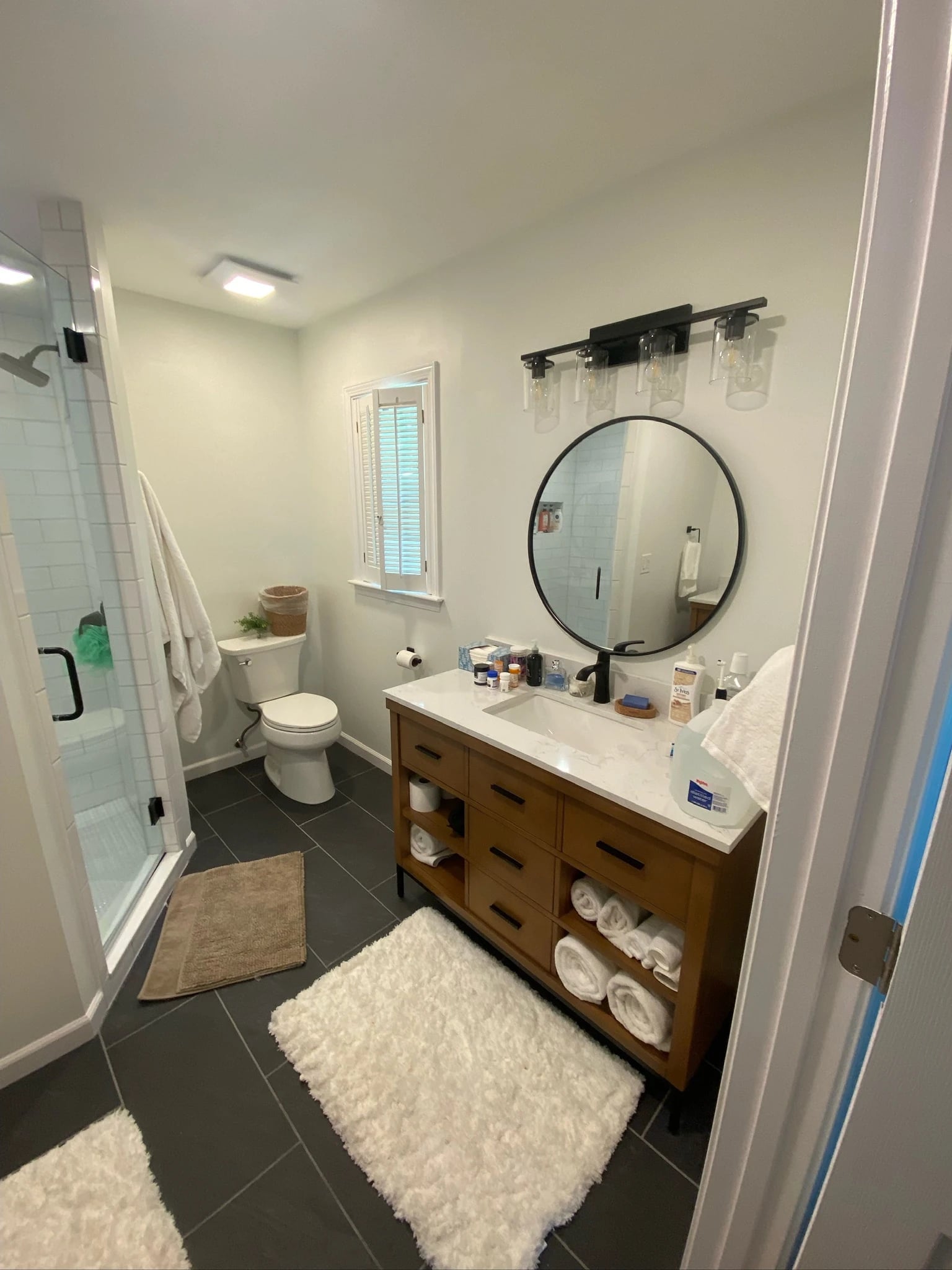 Wood vanity with open towel shelves beside a glass shower and window
