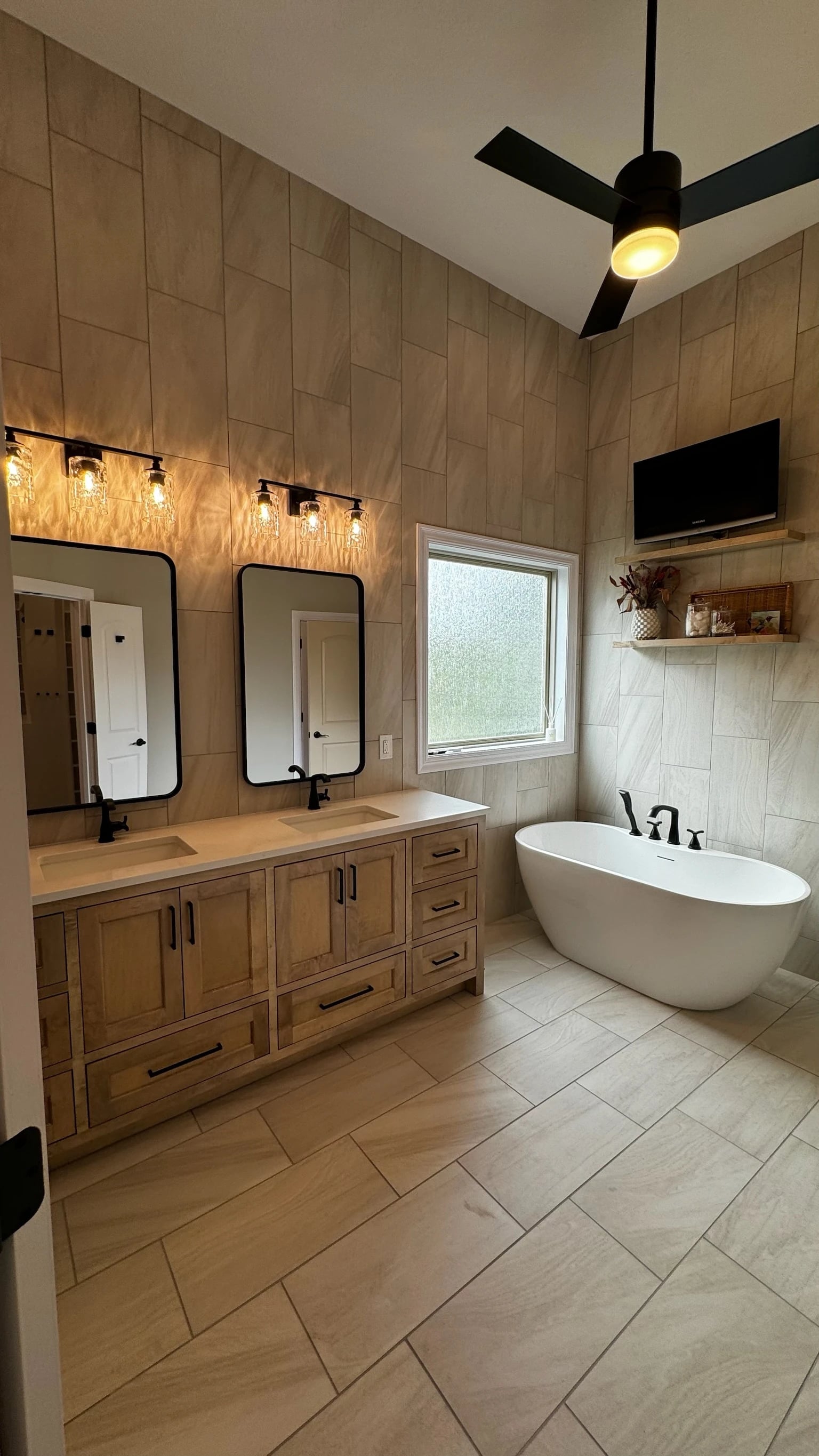 Custom wood double vanity and soaking tub beneath tall tile walls